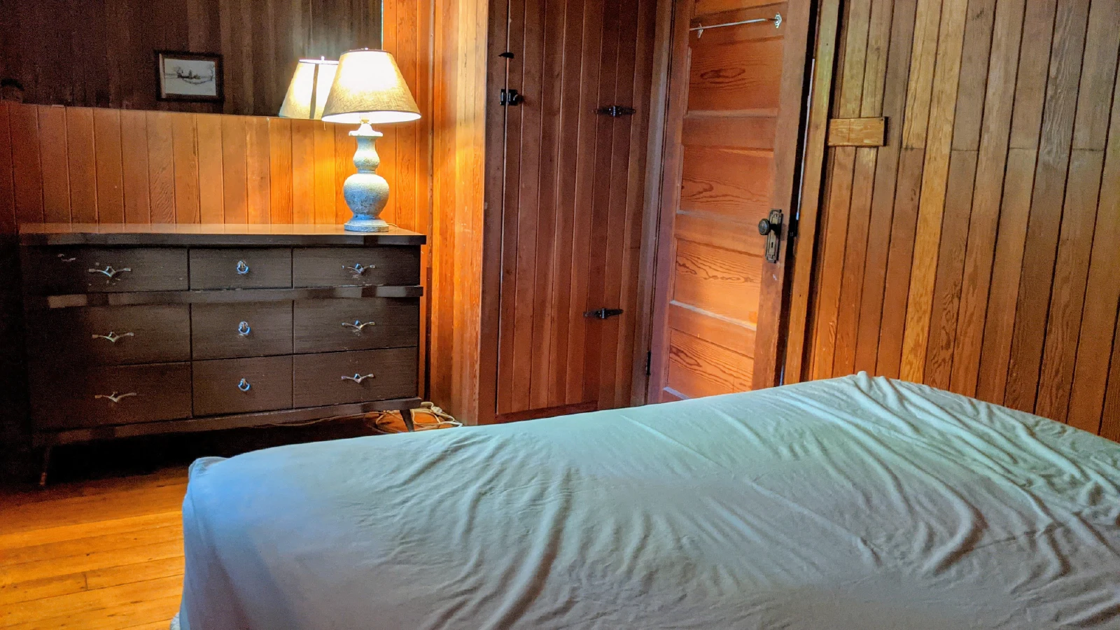 Pigeon Lake Resort Cottage Six, main bedroom with queen bed, wooden dresser, lamp, and wood-paneled walls